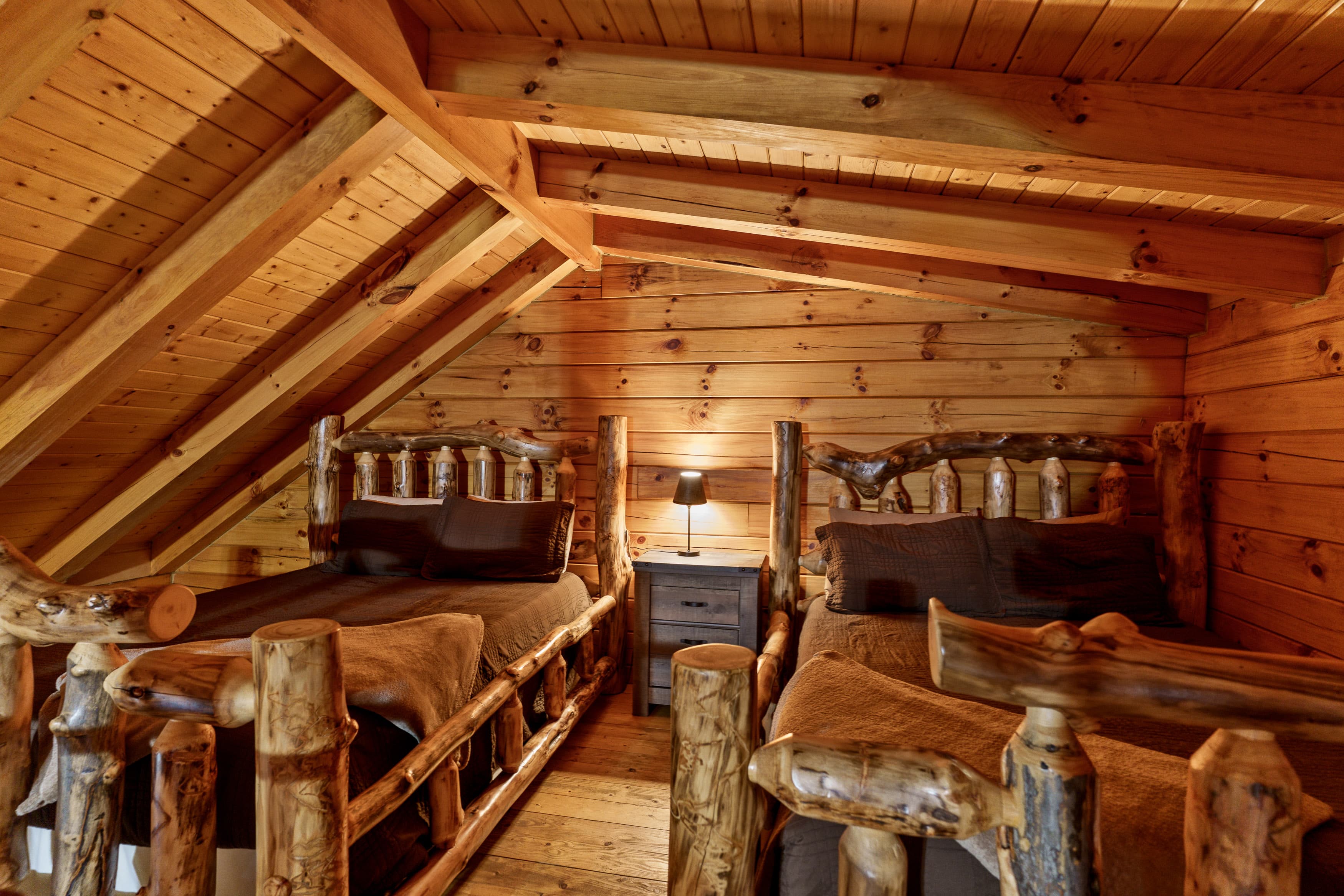 A cozy wooden attic bedroom featuring two rustic beds and soft lighting.