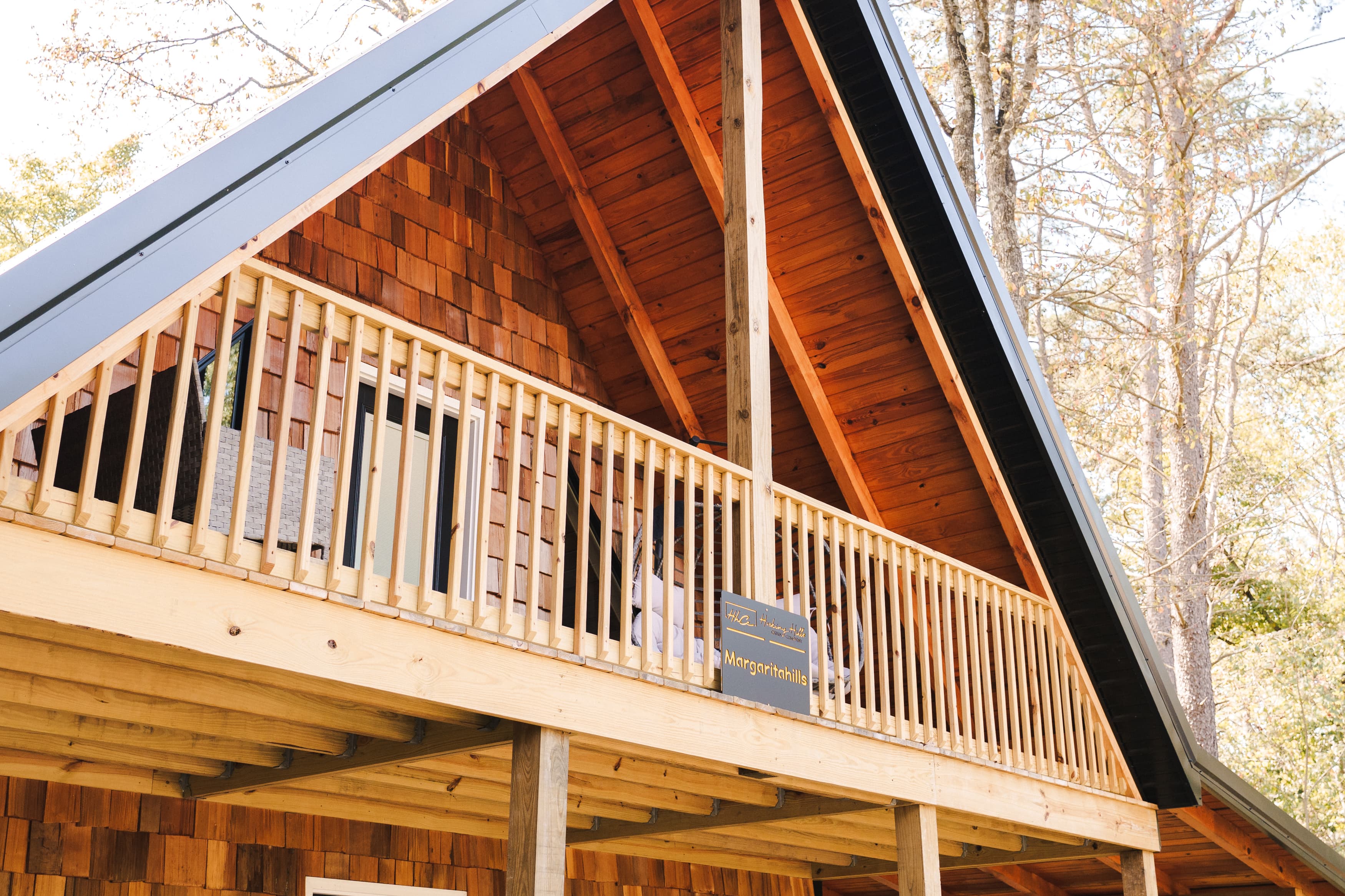 A wooden cabin with a sloped roof and a balcony overlooking a forested area.
