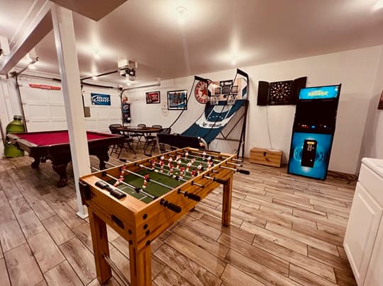 A game room featuring a foosball table, pool table, basketball arcade, and a vending machine.