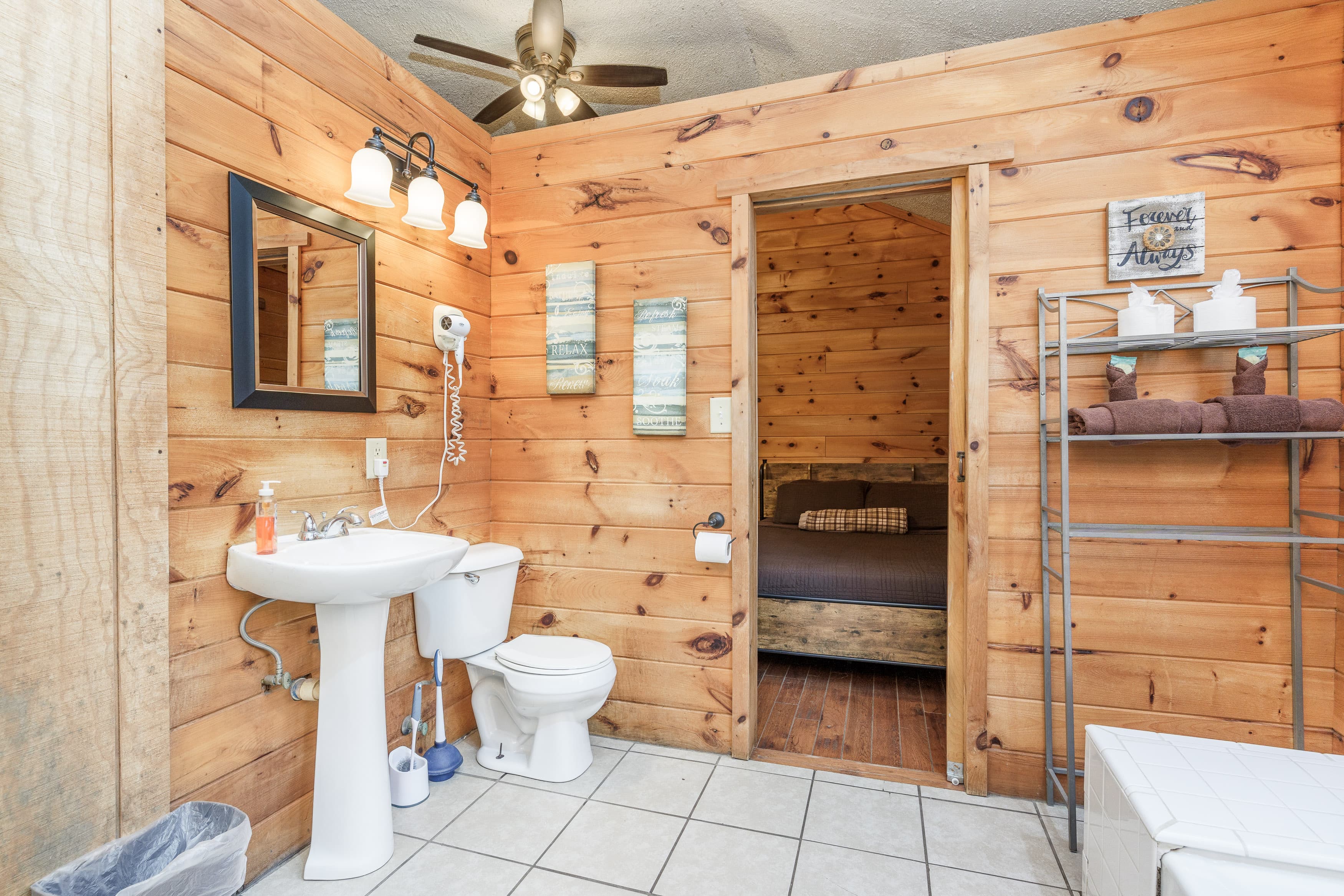 A cozy bathroom with wooden walls, a sink and toilet, and a doorway leading to a bedroom.