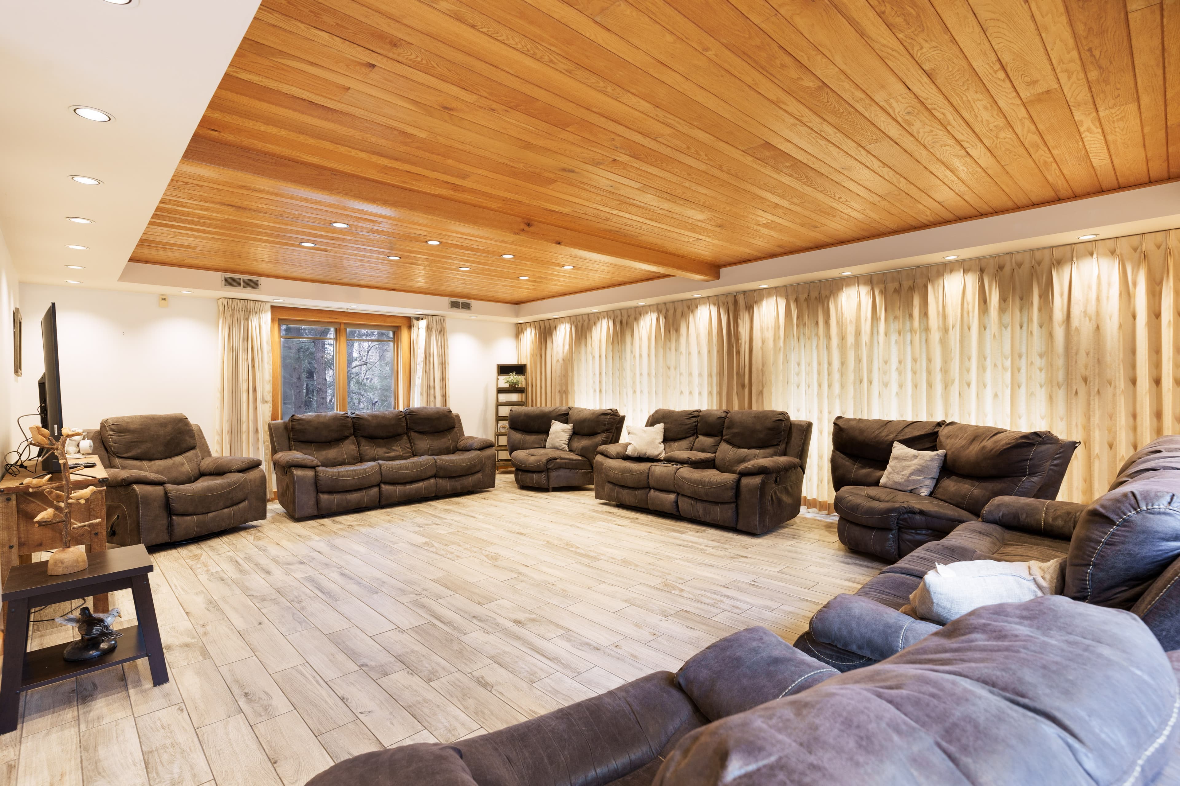 Spacious living room featuring multiple brown recliners and wooden ceiling accents.