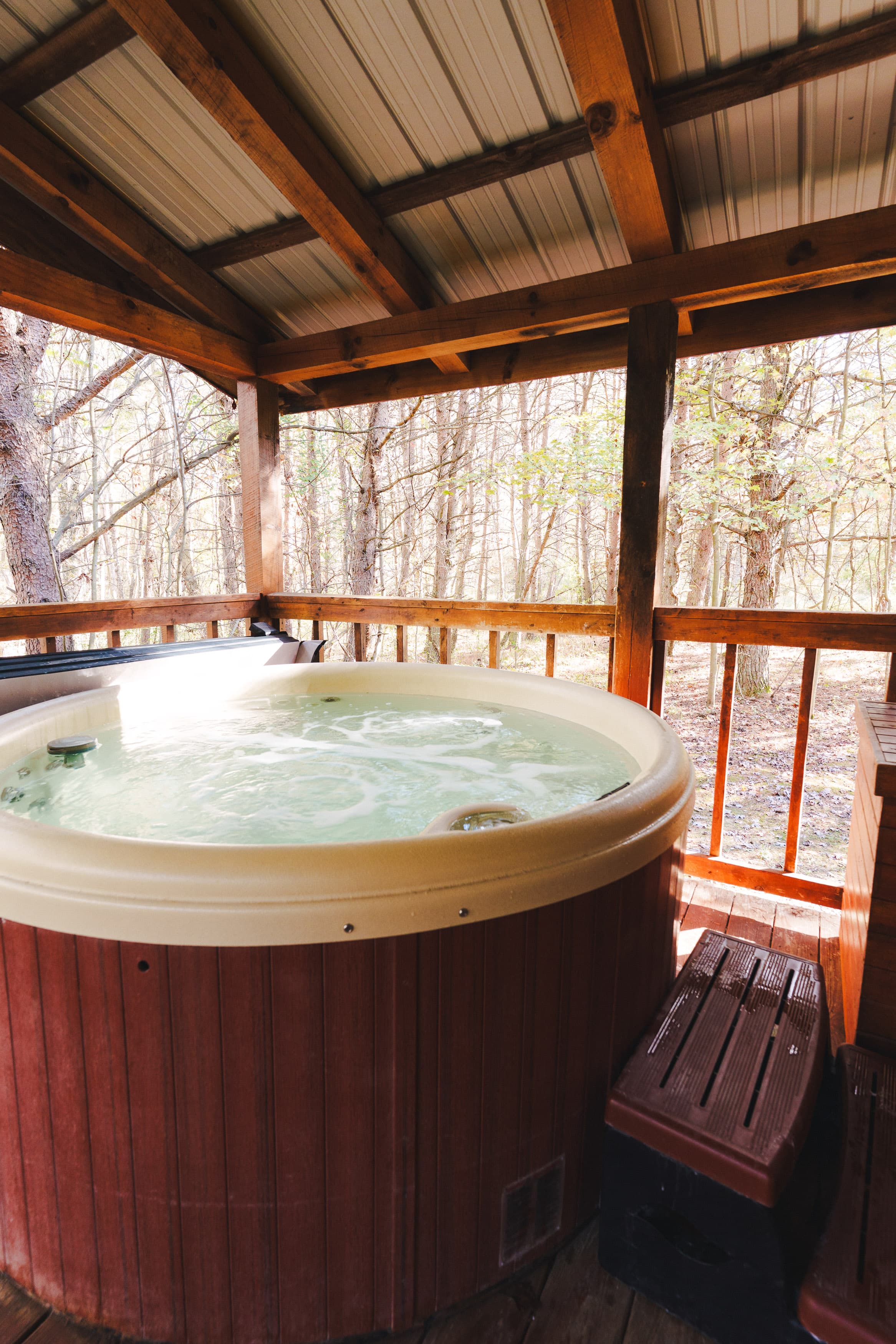 A wooden hot tub under a shelter surrounded by trees.