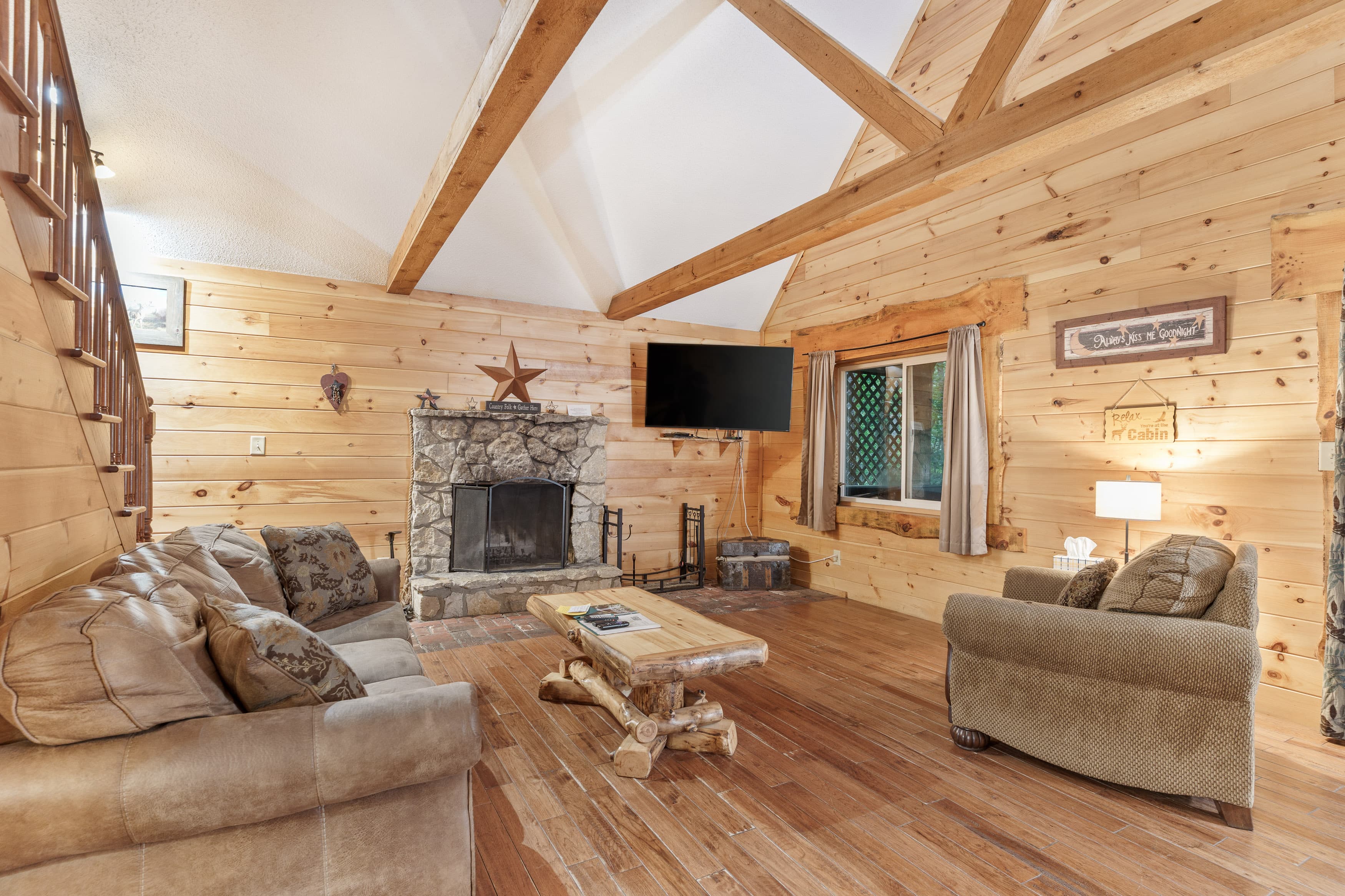 Cozy living room with wood-paneled walls, a stone fireplace, and rustic furnishings.