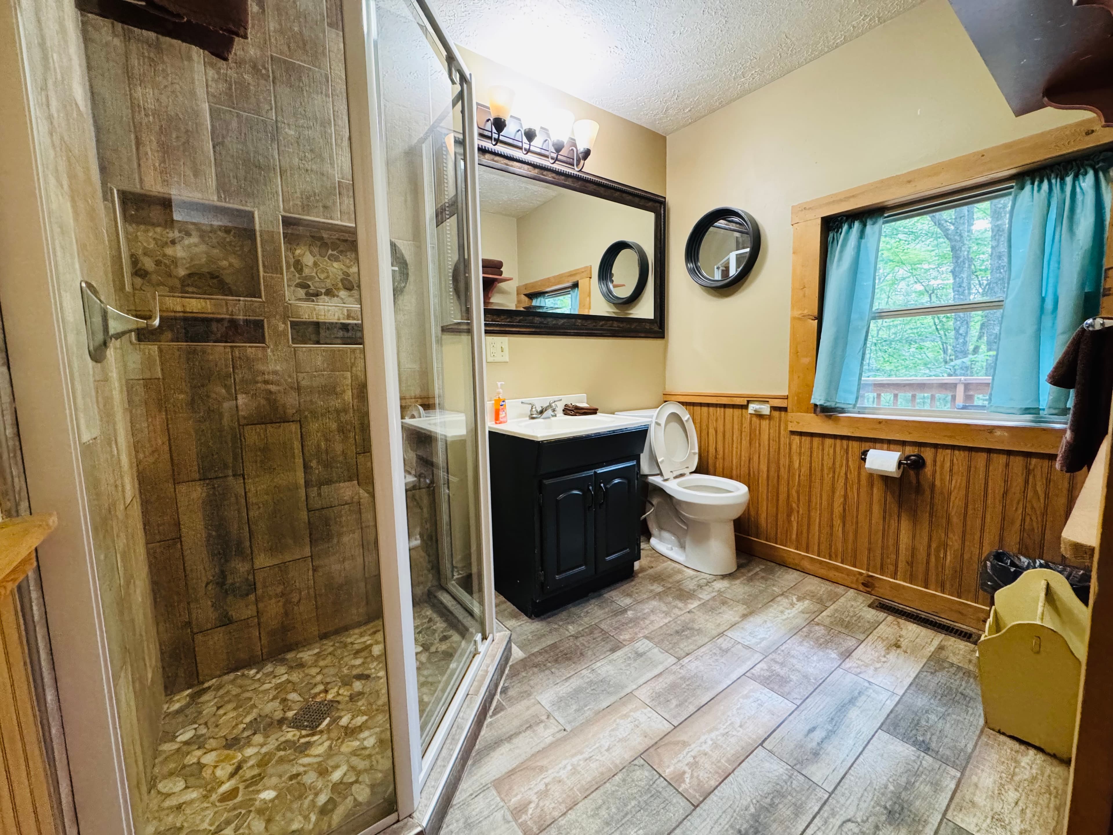 A modern bathroom featuring a glass shower, dark vanity, and wooden accents.