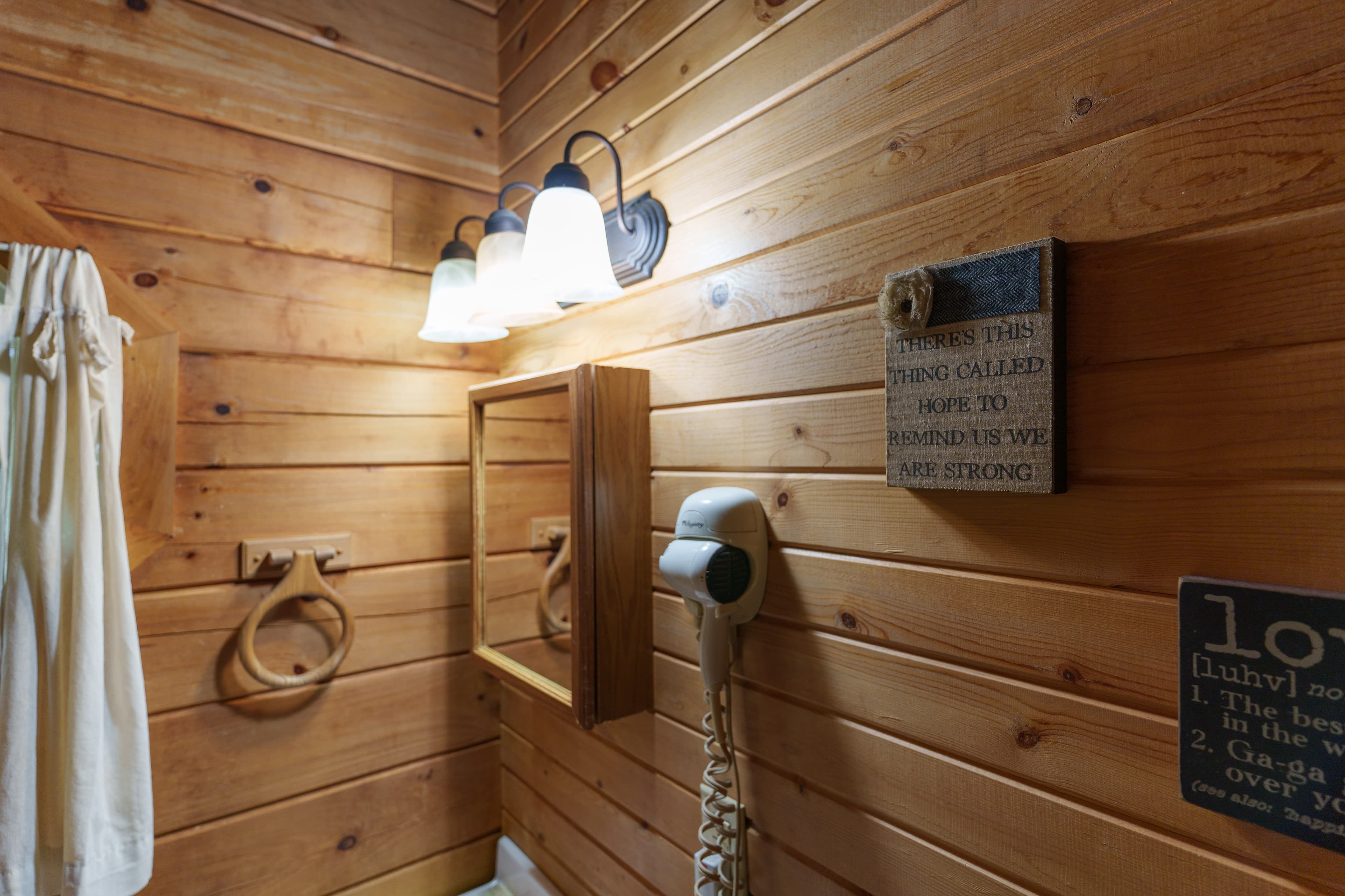 A cozy wooden bathroom with light fixtures, a mirror, a hand dryer, and motivational wall art.