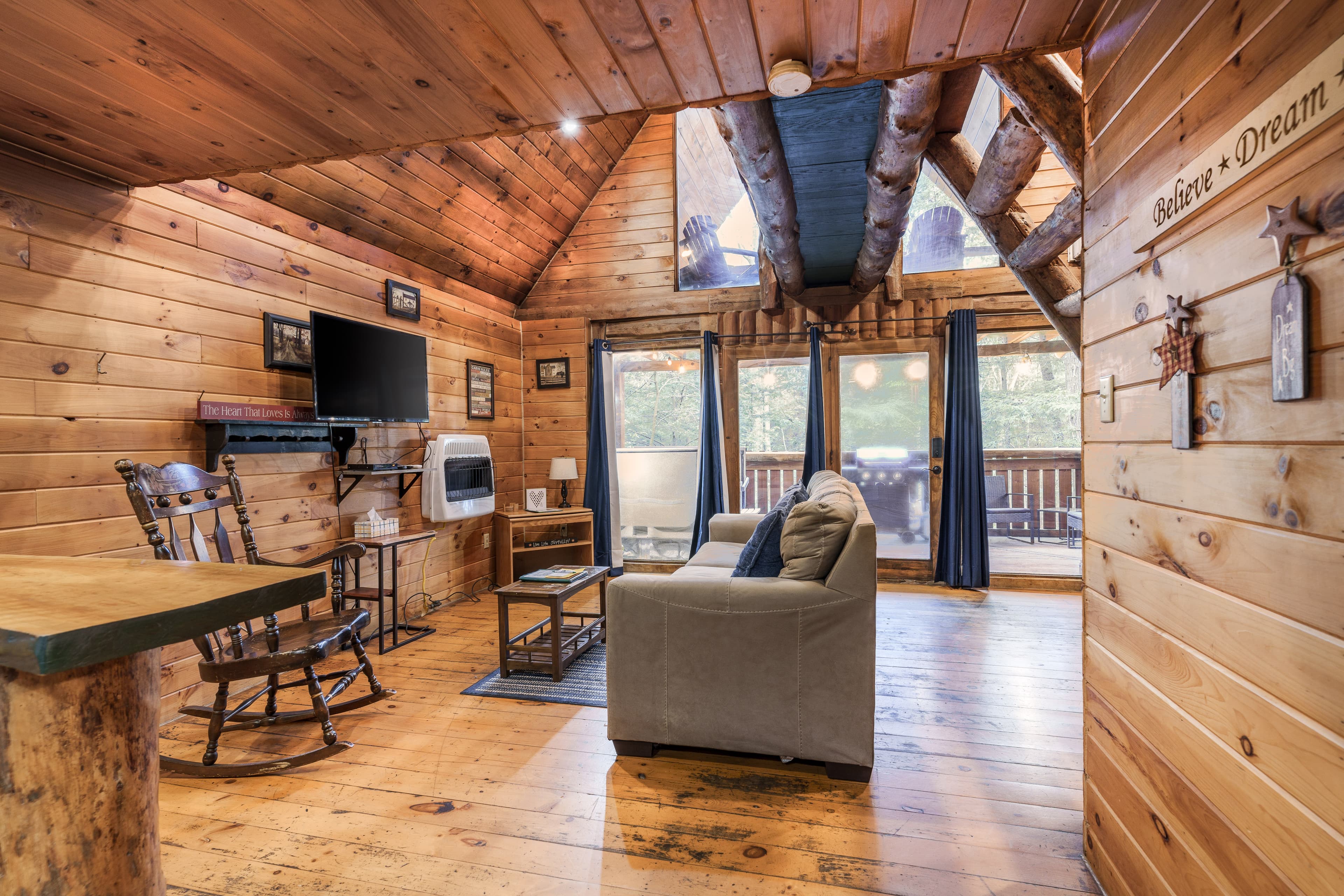 Cozy wooden cabin interior featuring a living area with a comfortable couch, a rocking chair, and large windows.