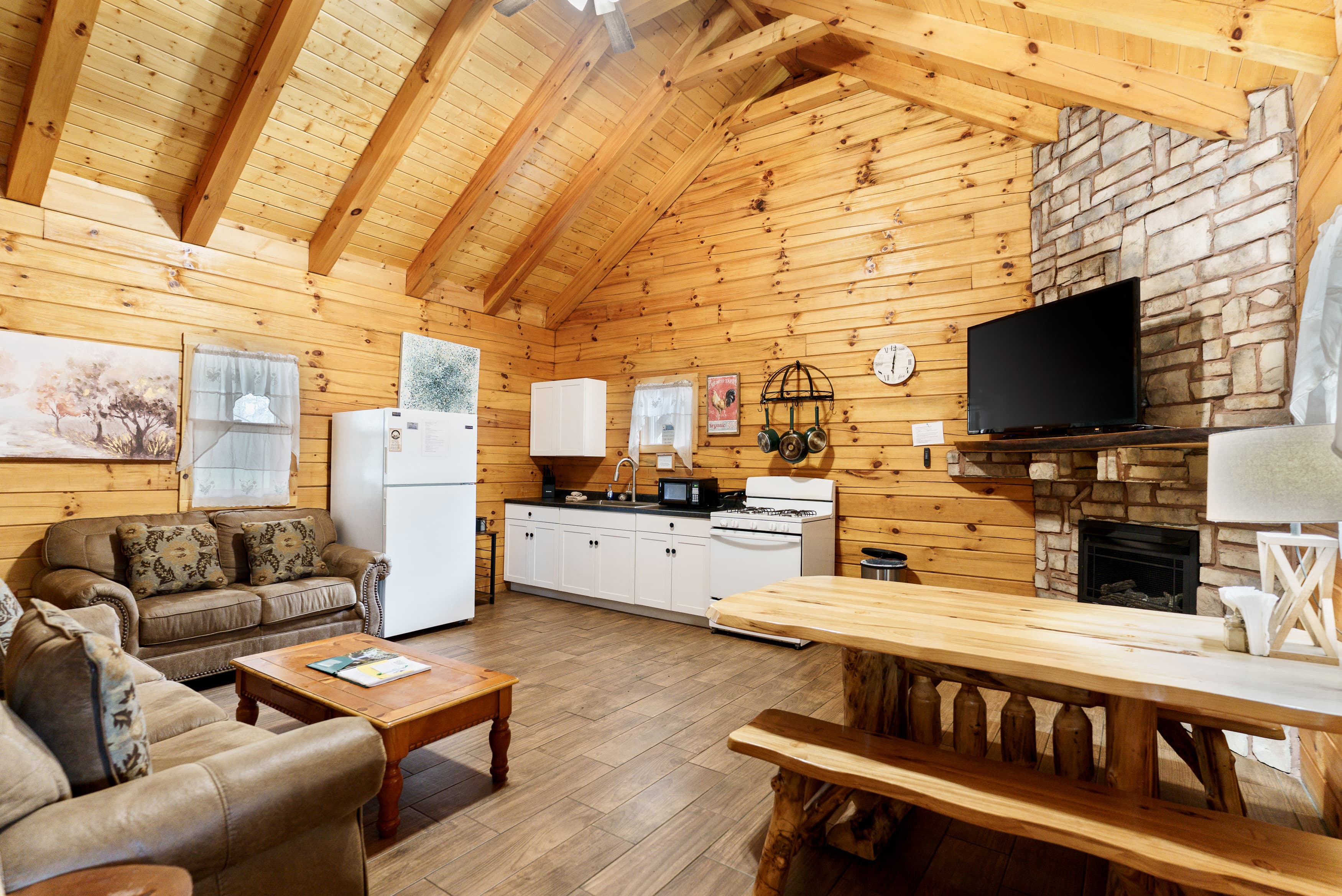 Cozy wooden cabin interior featuring a living area with a sofa, dining table, and kitchen appliances.