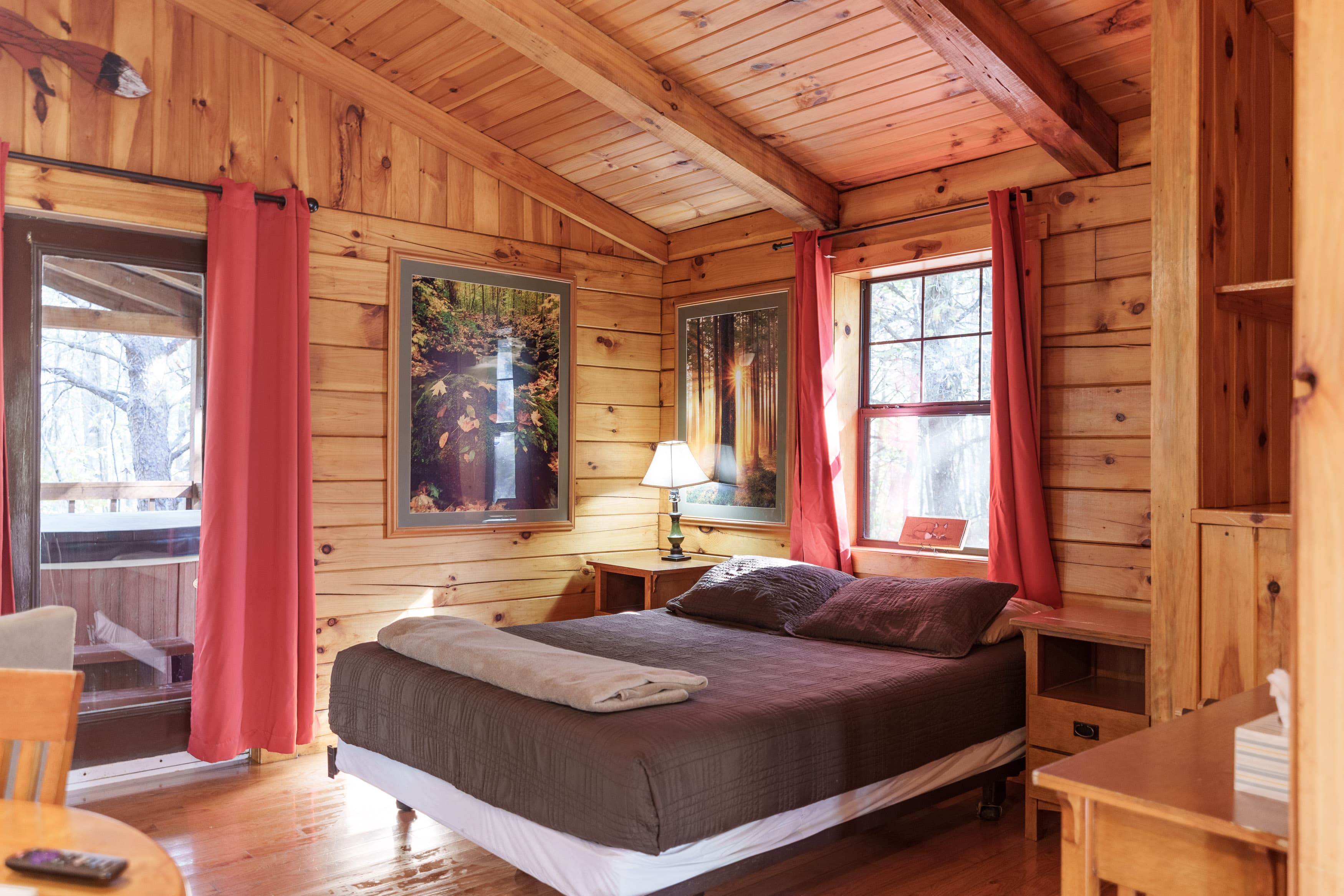 Cozy wooden bedroom with a double bed, red curtains, and natural light through the windows.