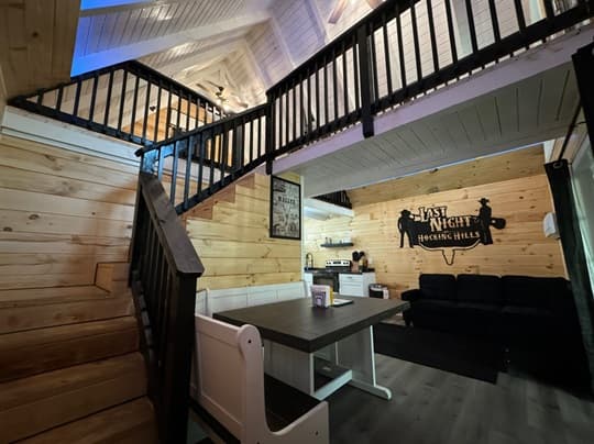 A cozy wooden interior with a dining area, staircase, and living space featuring a dark couch and decorative wall art.