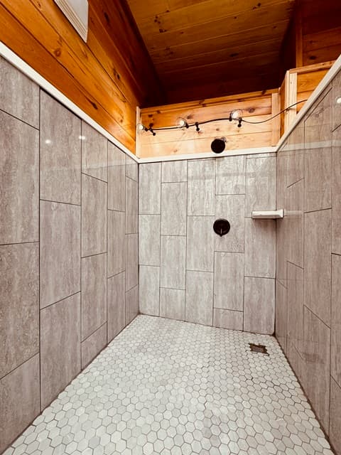 A spacious, modern shower with gray tiled walls and a hexagon tiled floor.