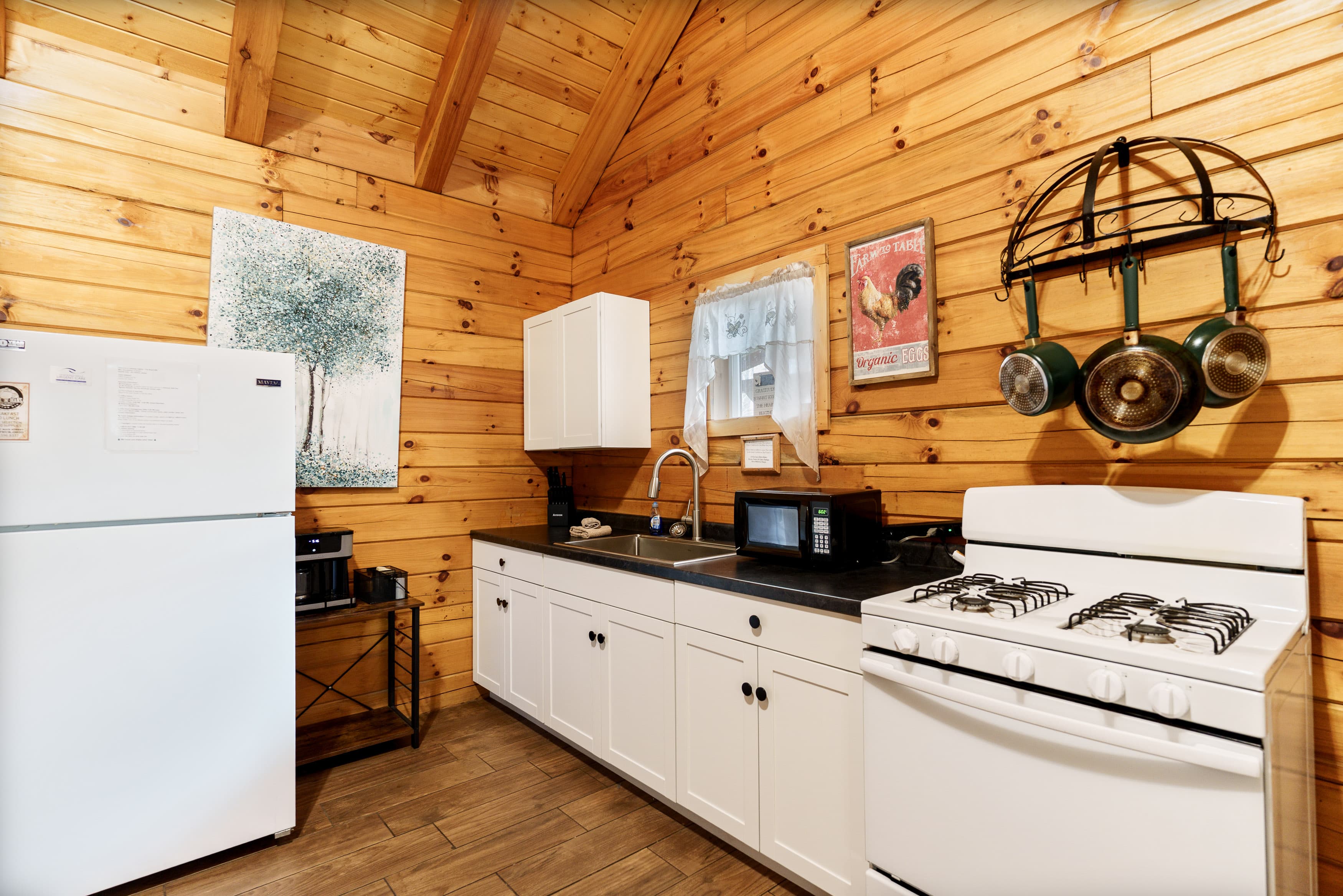 A cozy kitchen featuring wooden walls, white cabinetry, a gas stove, and modern appliances.