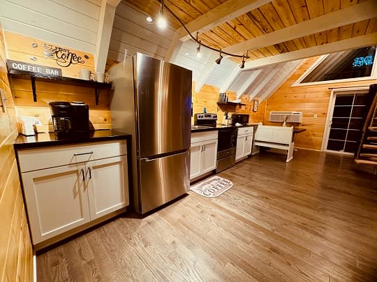 A cozy kitchen featuring wooden beams, a coffee bar, modern appliances, and warm, rustic decor.
