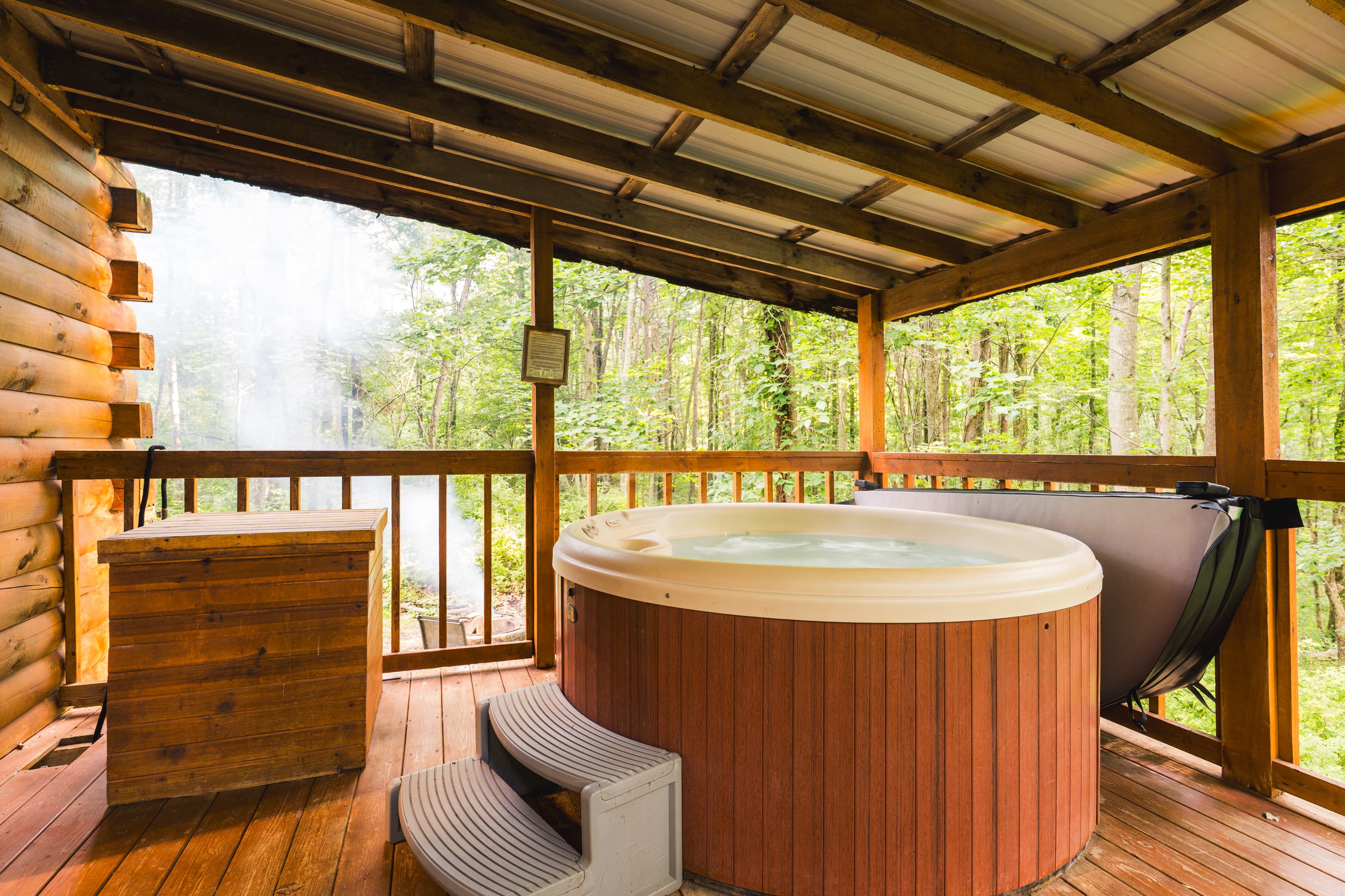 A hot tub on a wooden deck surrounded by trees and a rustic cabin setting.
