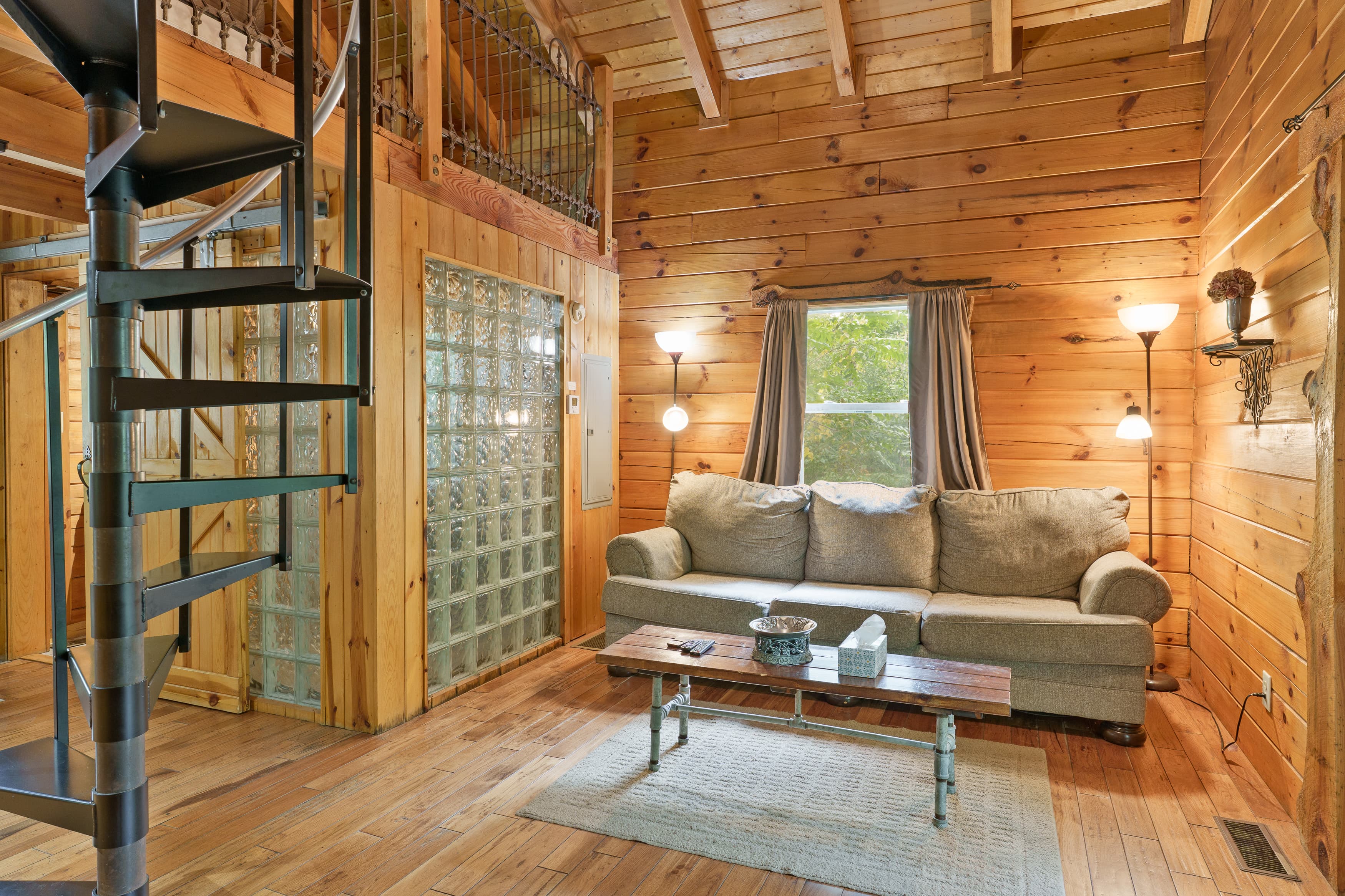 Cozy wooden living room featuring a spiral staircase, comfortable sofa, and a wooden coffee table.
