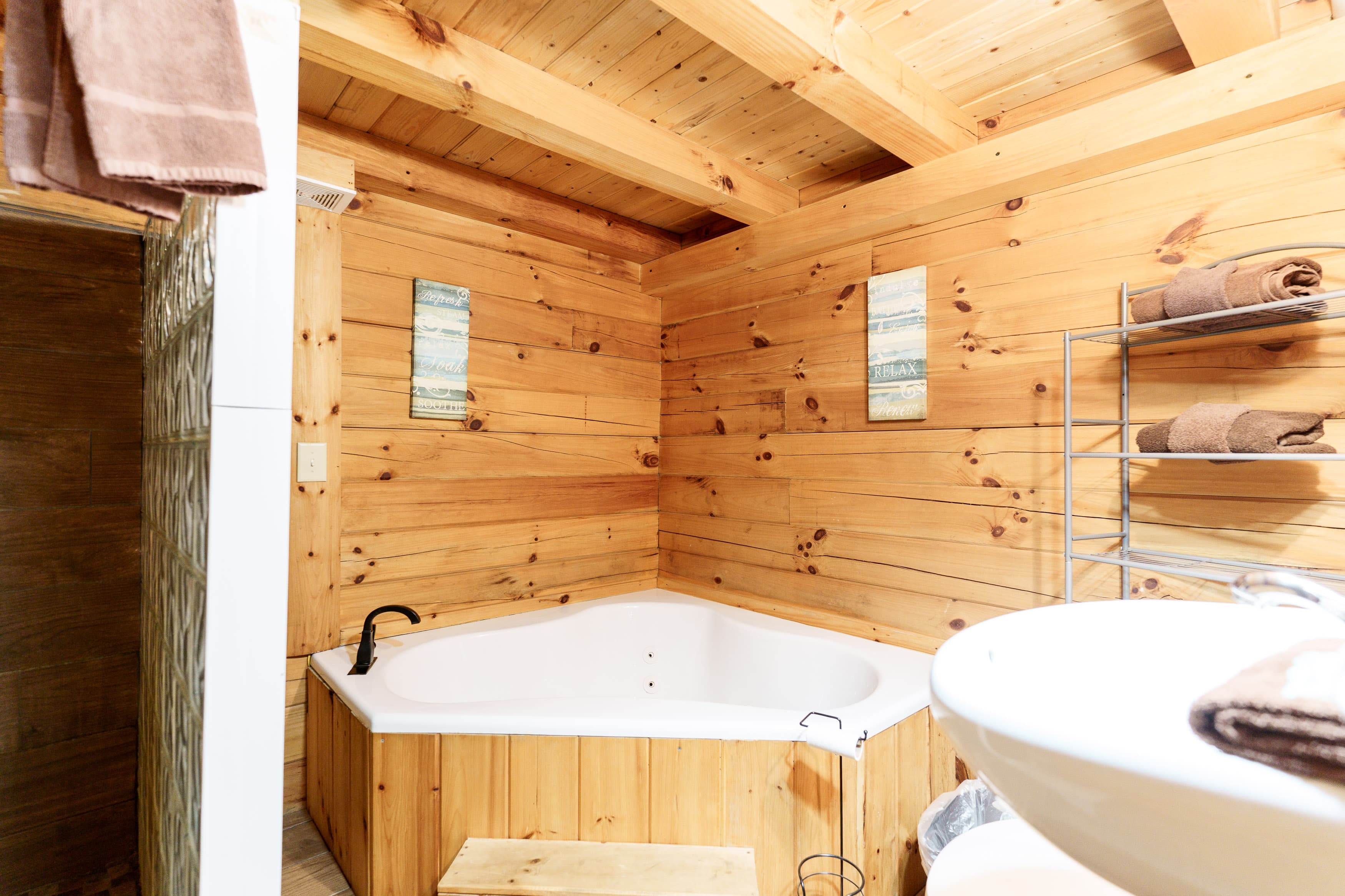 Cozy wood-paneled bathroom featuring a jetted tub, a modern sink, and neatly arranged towels.