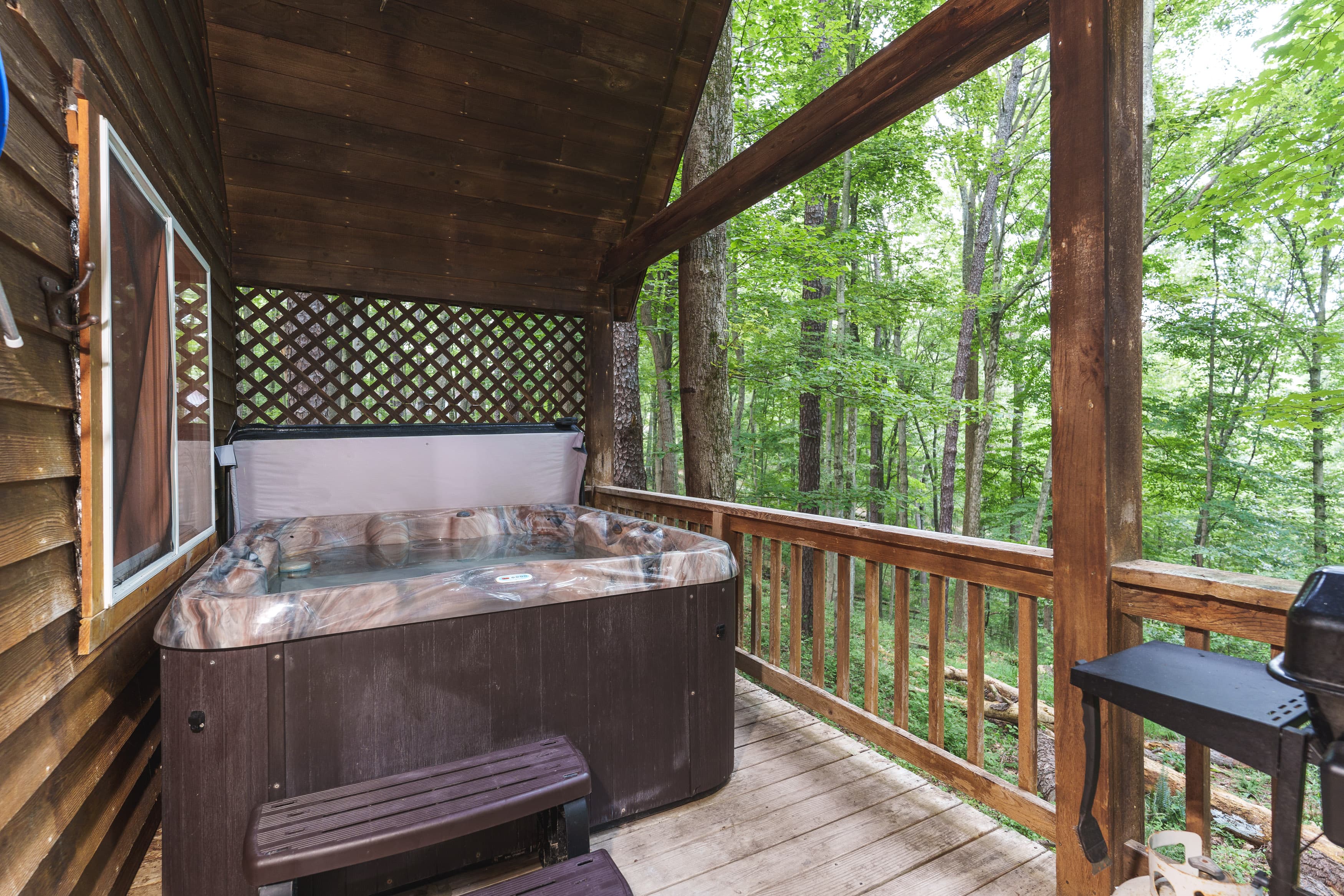 Hot tub on a wooden deck surrounded by lush green trees.
