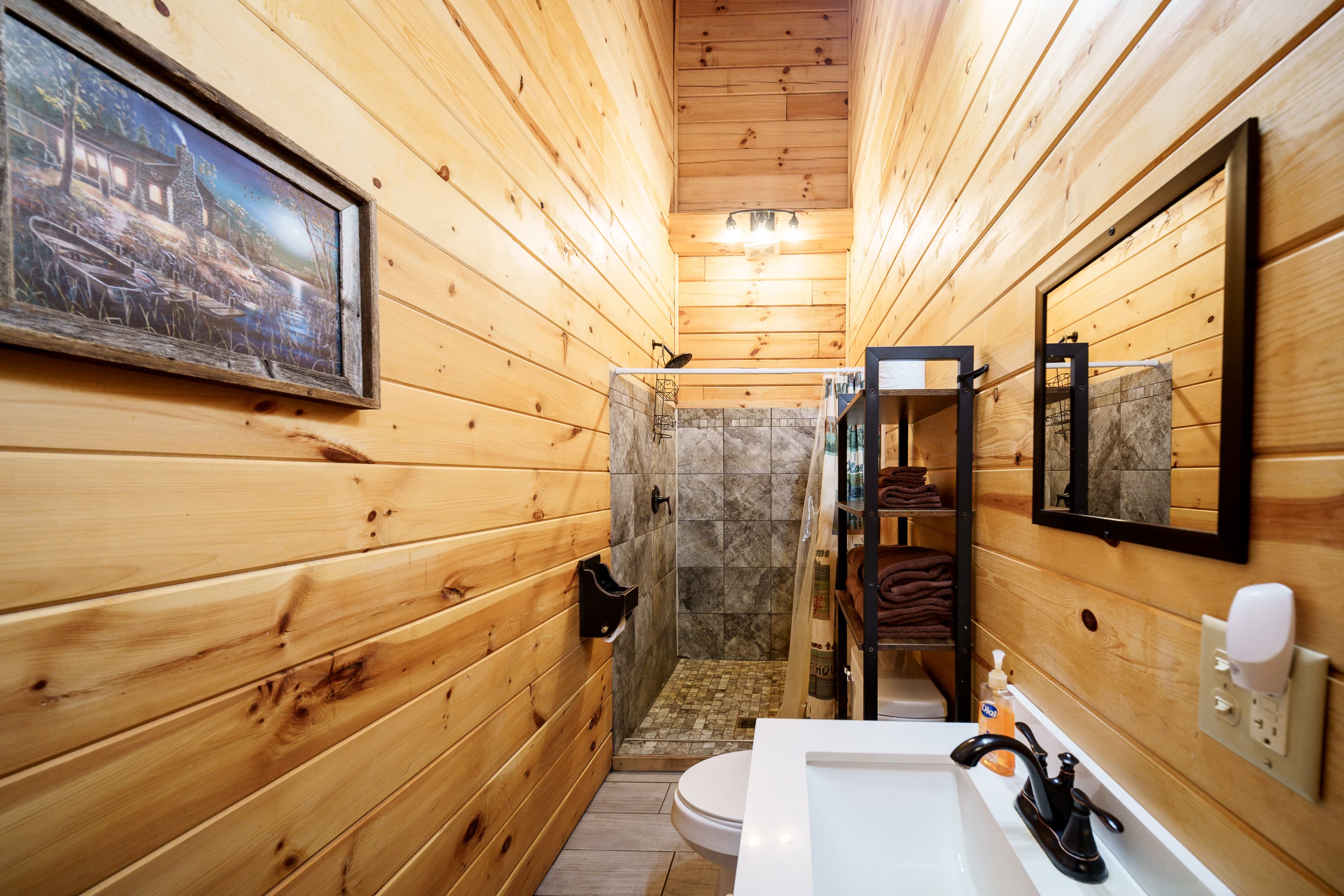 A cozy bathroom featuring wooden walls, a shower with tile accents, and a sink with modern fixtures.