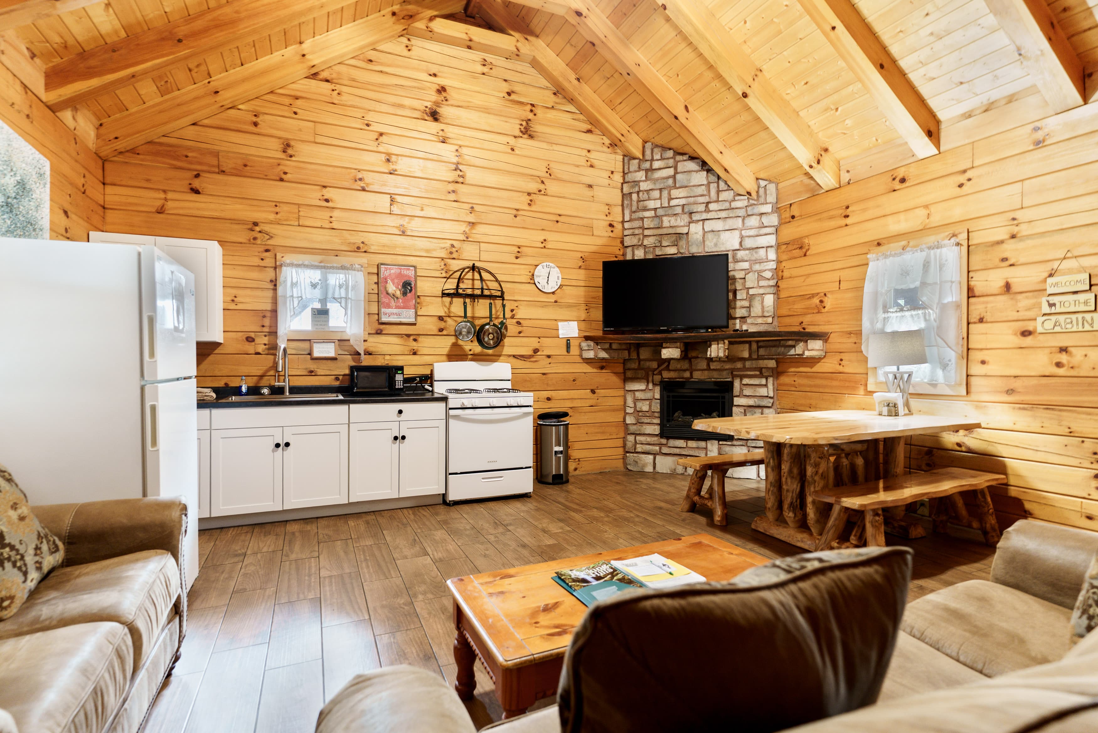 A cozy wooden cabin interior featuring a kitchen, dining area, and living space with a fireplace.