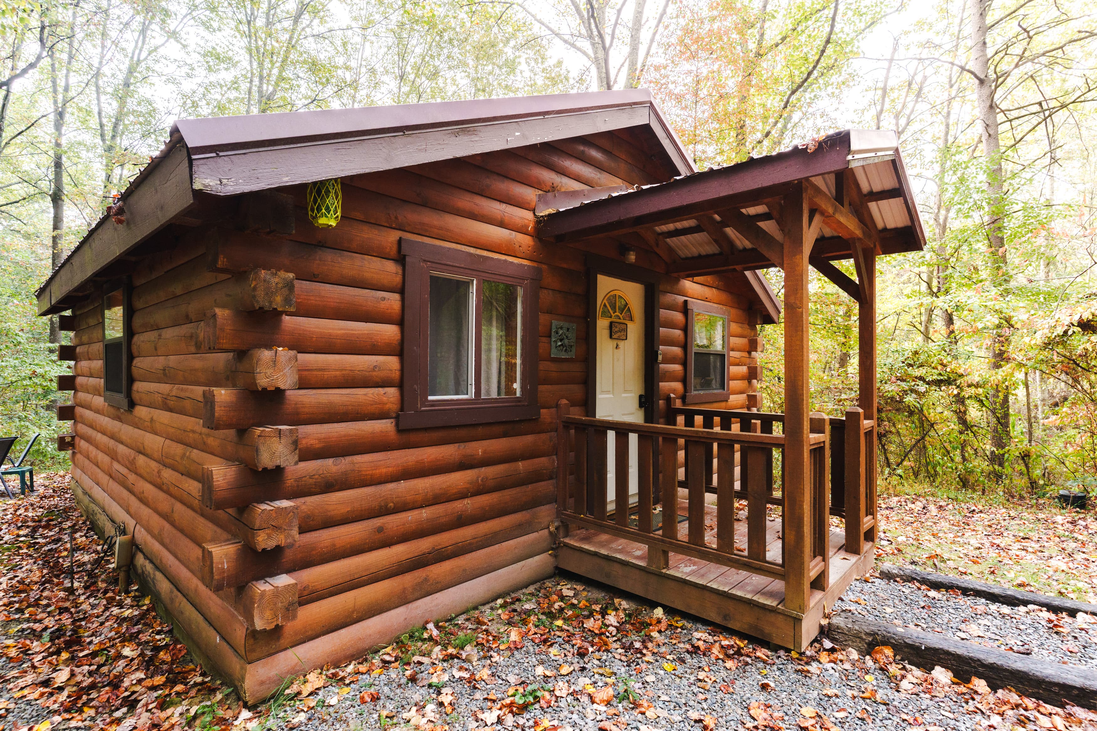 A rustic log cabin with a small porch surrounded by autumn foliage.