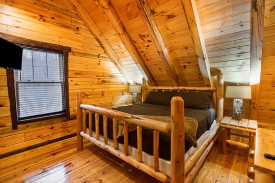 Cozy wooden bedroom with a log bed and sloped ceiling.