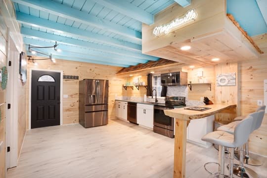 Bright, modern kitchen with light wooden walls, blue ceiling beams, and stainless steel appliances.