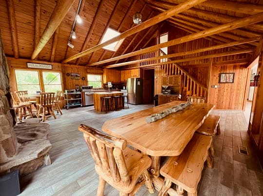 A rustic wooden kitchen and dining area with a large table, log-style furniture, and open beams.