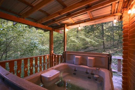 A hot tub on a wooden deck surrounded by lush green trees.