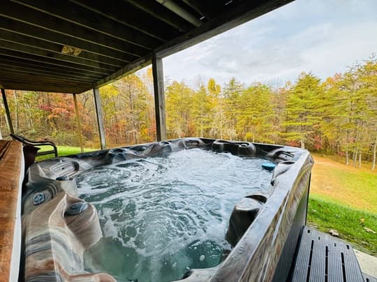 A hot tub with bubbling water is positioned on a deck overlooking colorful autumn trees.