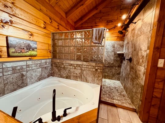 A cozy bathroom featuring a jetted tub and a tiled shower, with wooden accents and soft lighting.