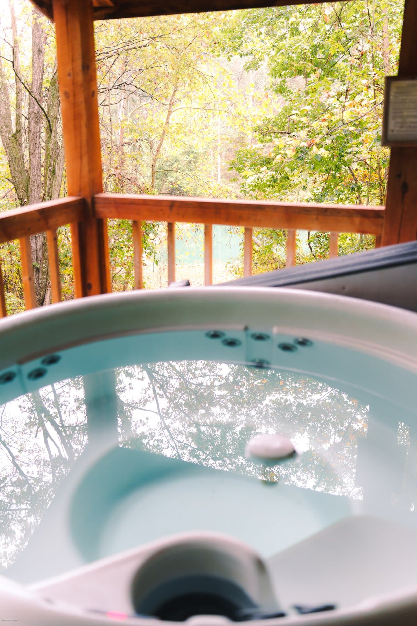 A hot tub sits on a wooden deck overlooking a serene, tree-filled landscape.