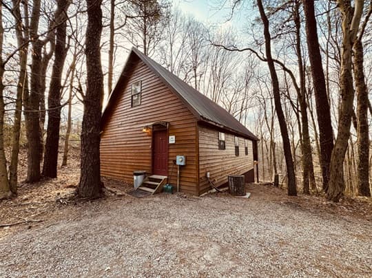 A wooden cabin surrounded by bare trees and gravel path.