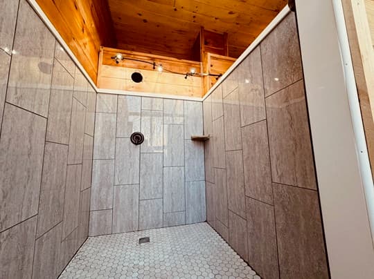 A spacious shower with gray tile walls and a hexagonal tiled floor.