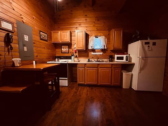 Cozy kitchen with wooden walls, equipped with cabinets, a stove, a refrigerator, and a small dining table.