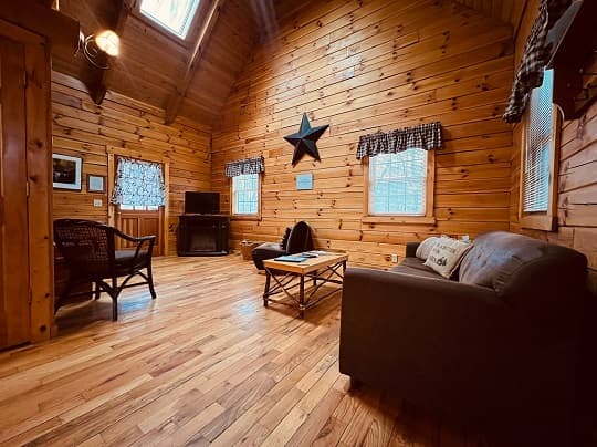 Cozy wooden interior of a cabin living room featuring a sofa, chairs, and large windows.