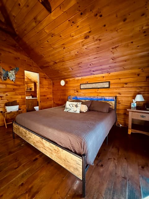 Cozy bedroom with a wooden interior, featuring a bed, nightstand, and decorative elements.