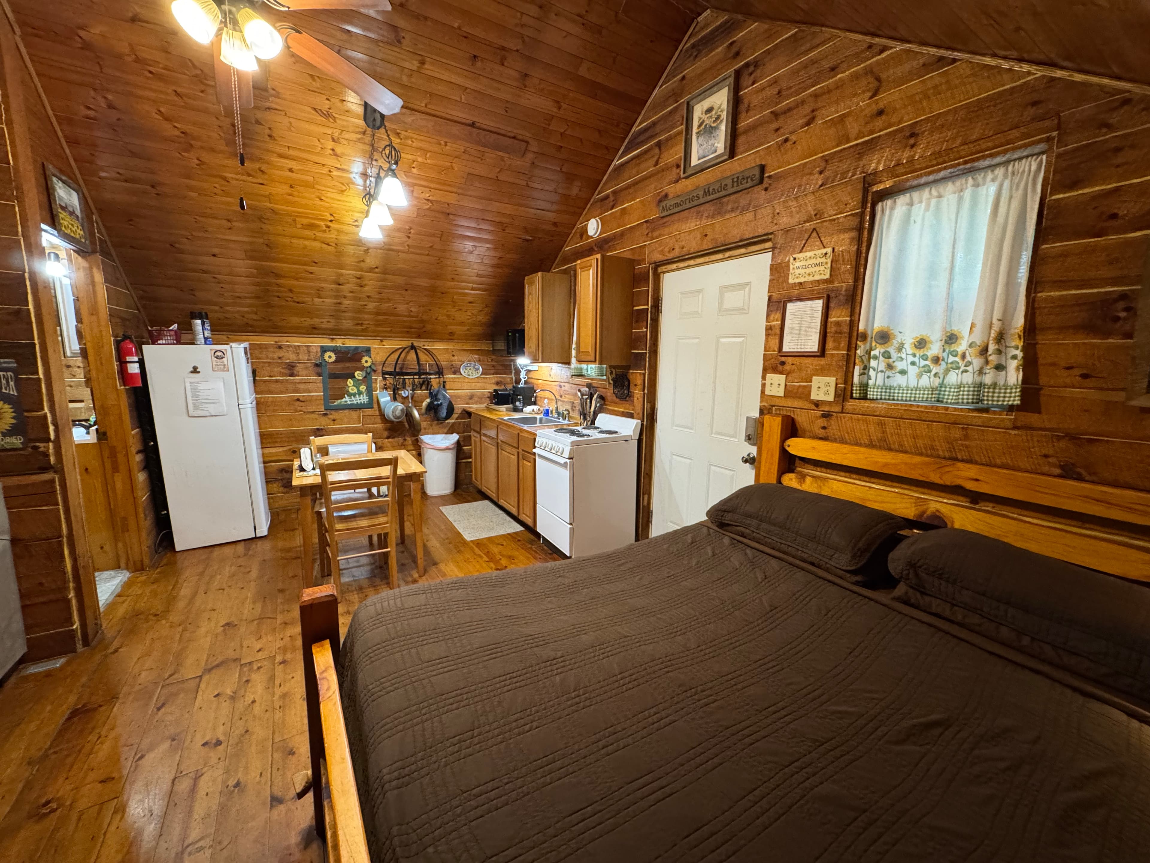 A cozy cabin interior featuring a wooden bed, kitchenette, and dining area under a sloped ceiling.
