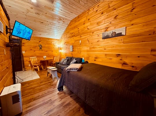 Cozy wooden cabin interior featuring a bed, dining table, and a flat-screen TV.