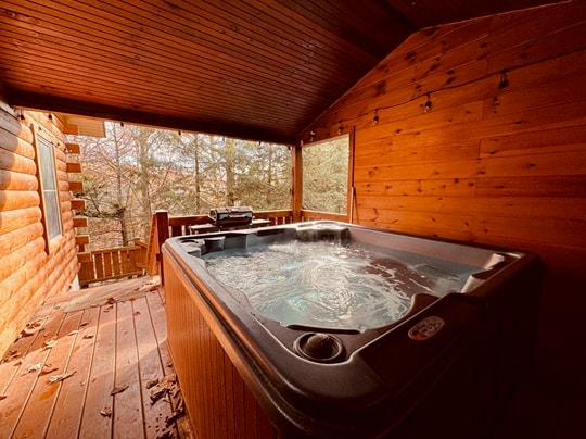 A hot tub on a wooden deck in a cozy cabin, surrounded by trees.