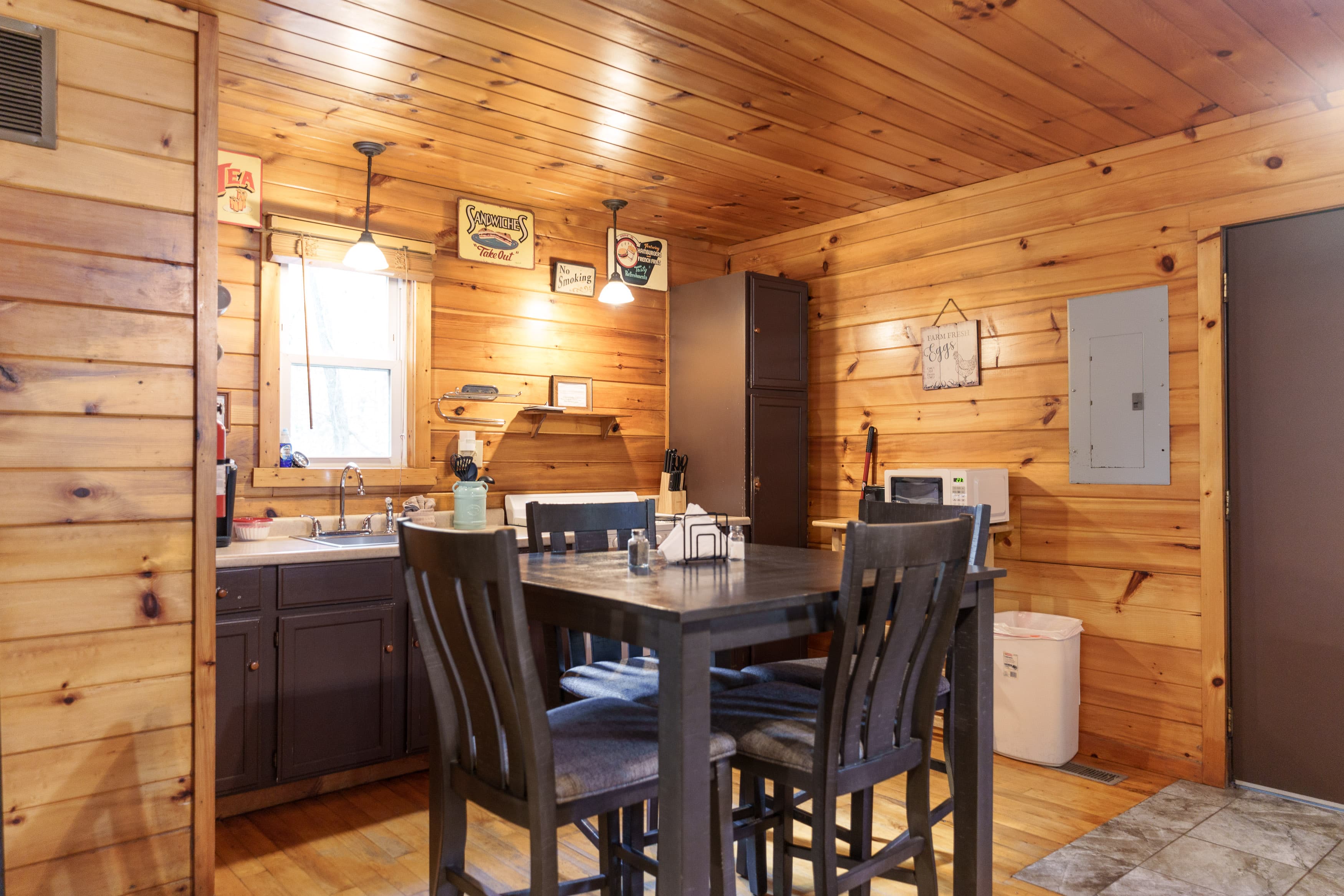 A cozy wooden kitchen featuring a dining table, chairs, and various kitchen appliances.