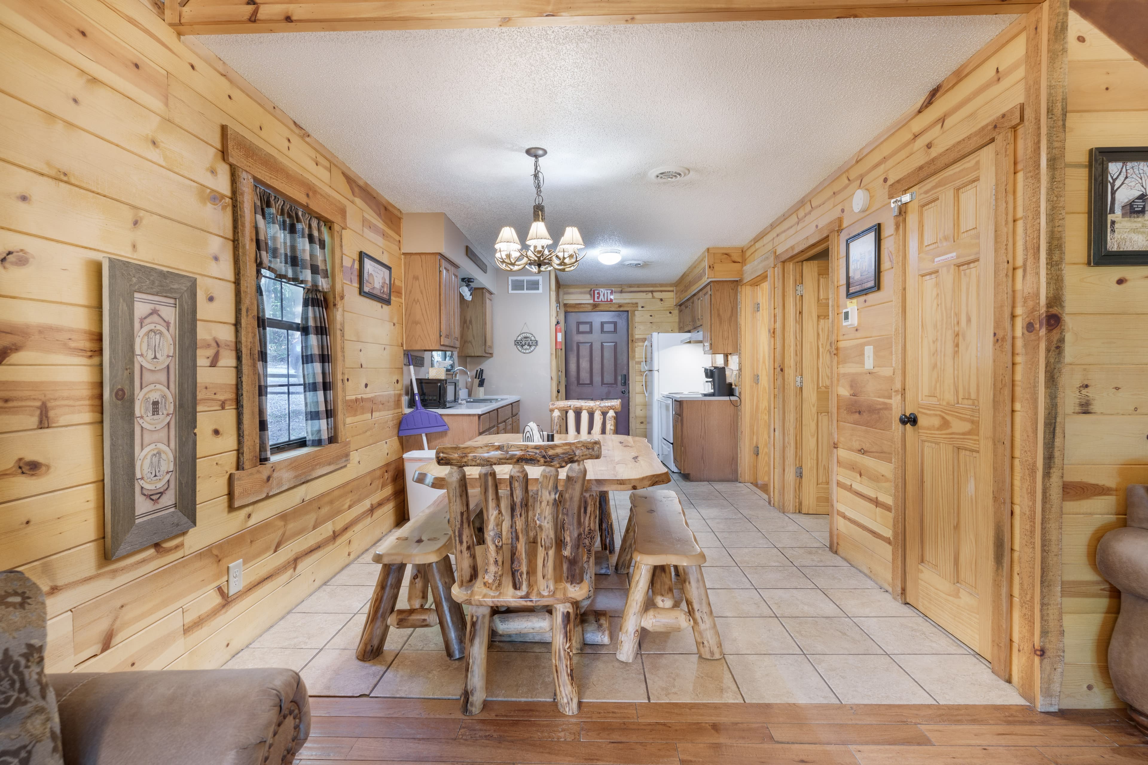 A rustic wooden dining area with a table and log-style chairs, leading into a kitchen with light wooden cabinetry.