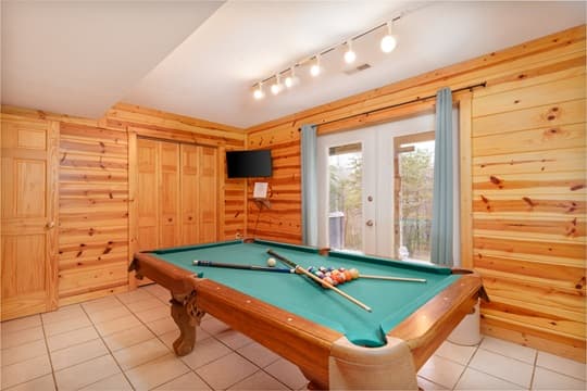 Cozy game room featuring a pool table and wooden walls.