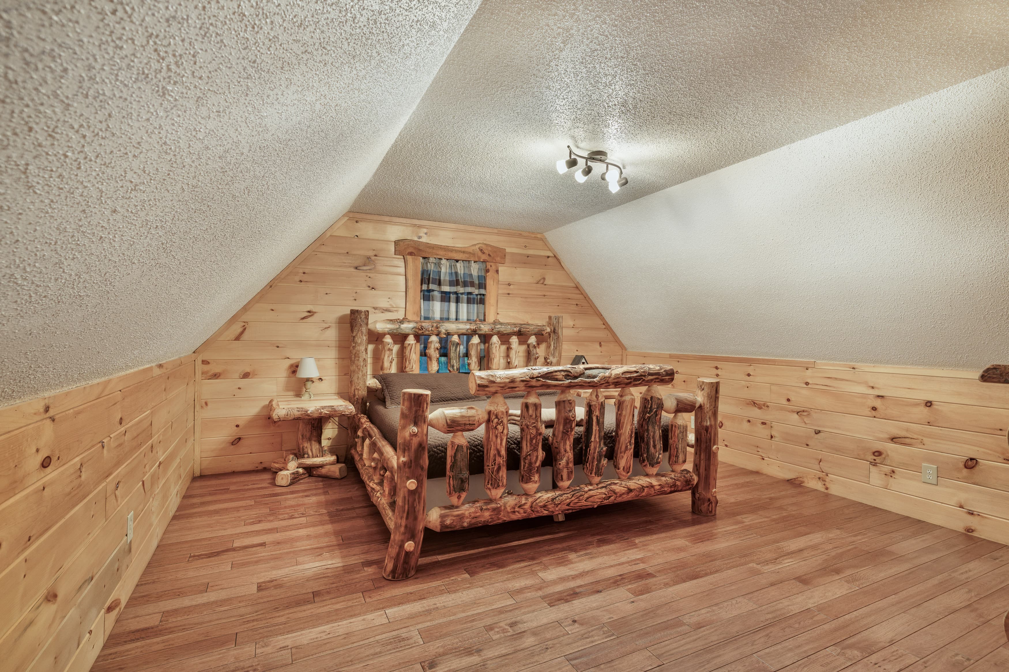 Cozy attic bedroom featuring a rustic log bed and wood-paneled walls.