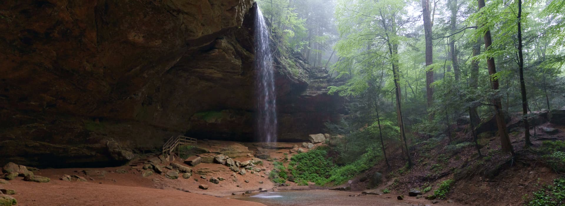 A serene forest scene featuring a cascading waterfall within a cave, surrounded by lush greenery.