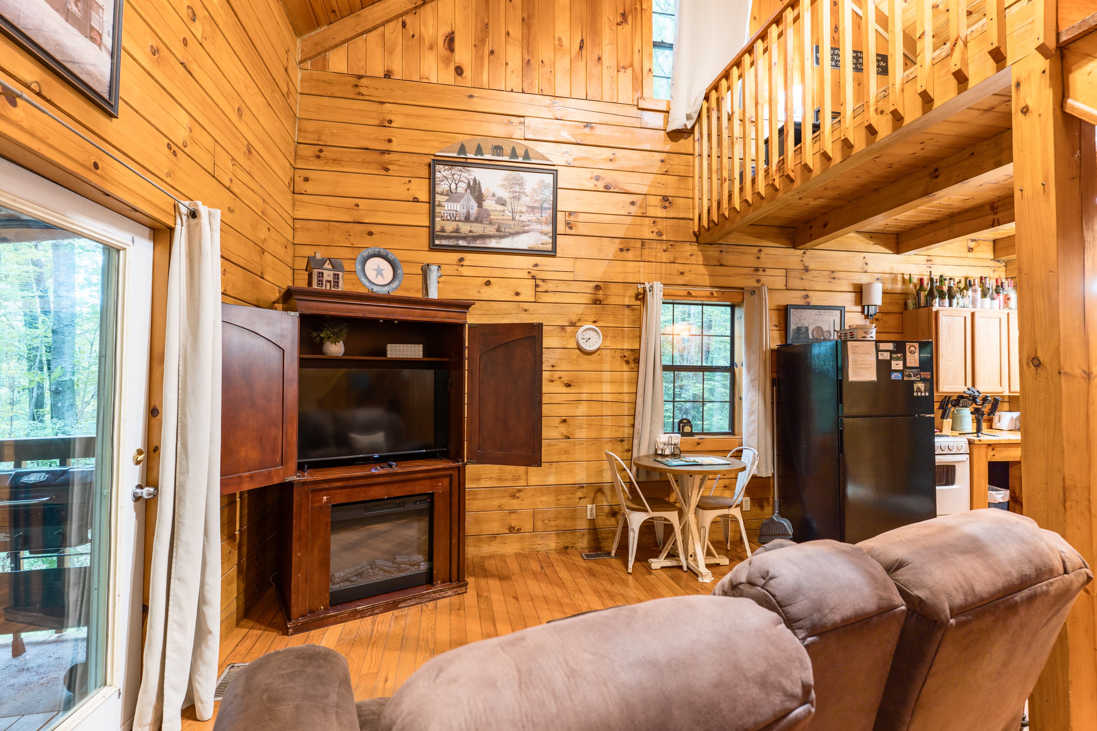 Cozy wooden cottage interior featuring a living area with a sofa, entertainment center, and kitchen.
