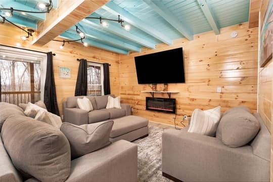 A cozy living room with two gray sofas, a mounted TV, and wooden walls featuring a blue ceiling.