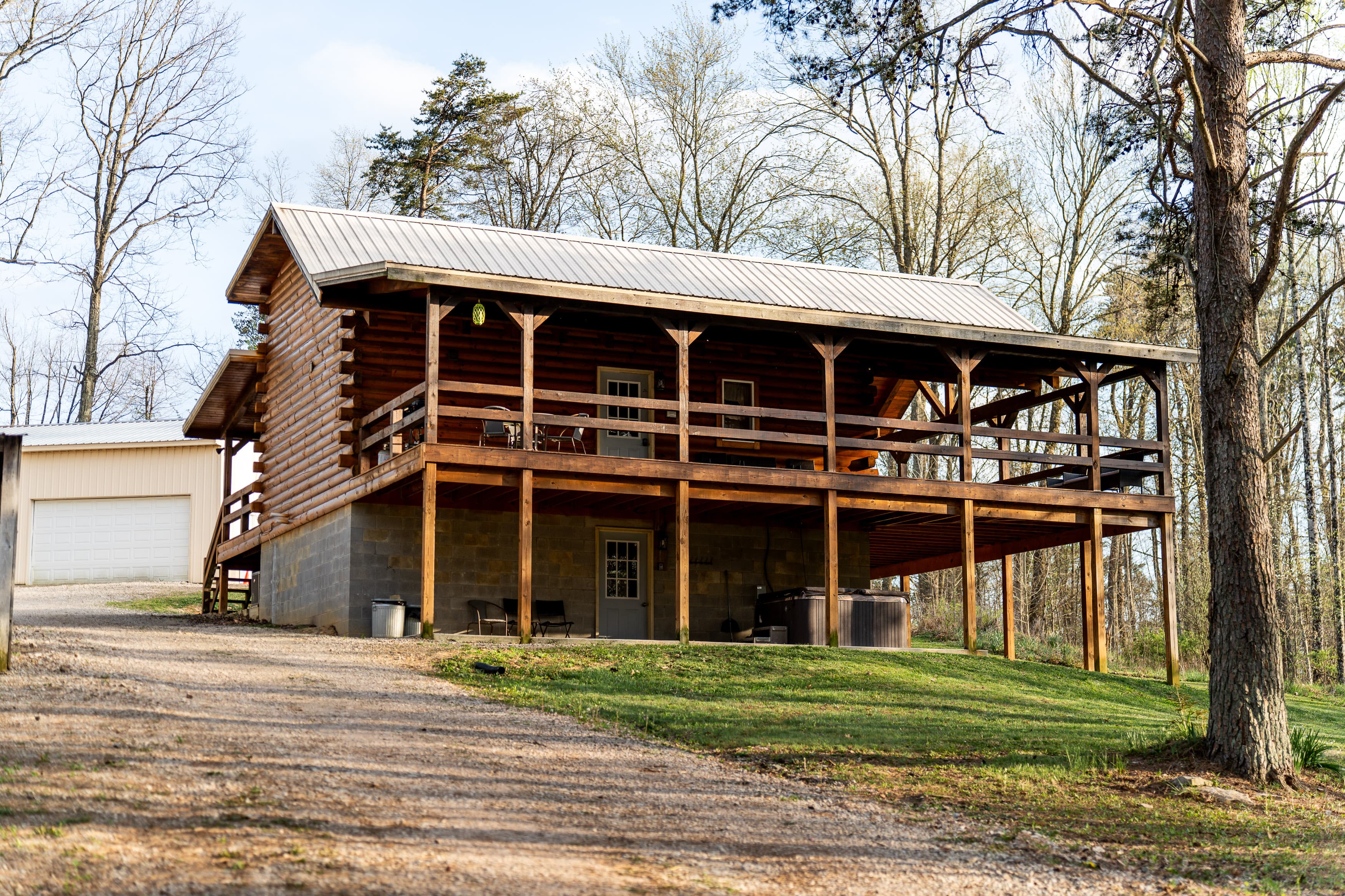 A rustic log cabin with a large porch sitting on a grassy lot surrounded by trees.