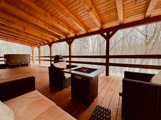 A cozy wooden patio with seating and a fire pit overlooking a winter forest.
