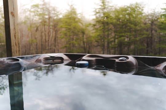 A hot tub sits on a deck, reflecting the surrounding trees and sky.