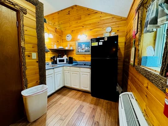 Cozy kitchen with wooden walls, white cabinetry, a black refrigerator, and various appliances.