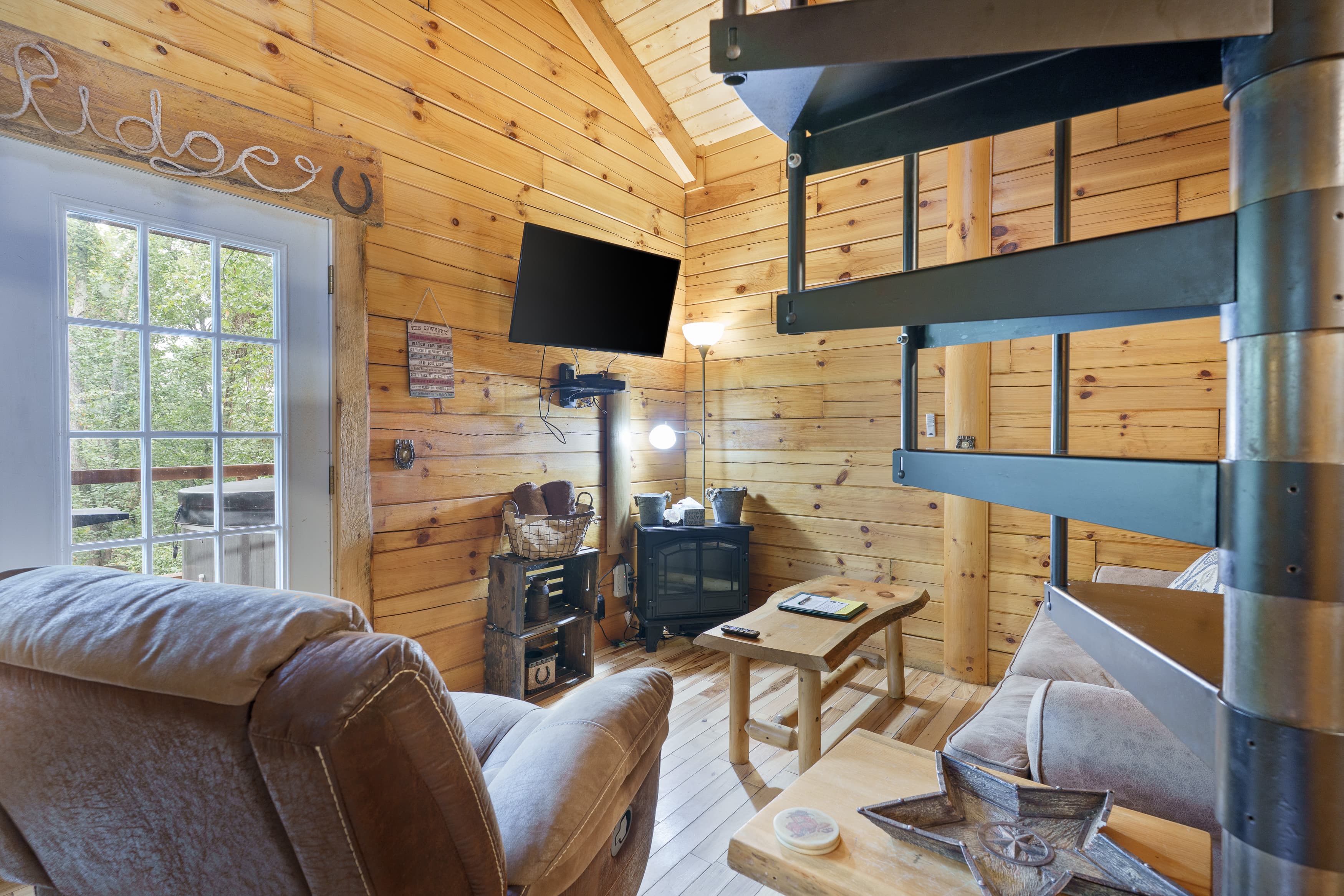 Cozy interior of a wooden cabin featuring a spiral staircase, comfortable seating, and a TV.